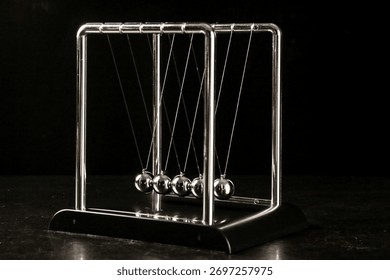 Newton's cradle pendulum demonstrating physics principles of momentum and energy transfer with suspended metal spheres on dark background