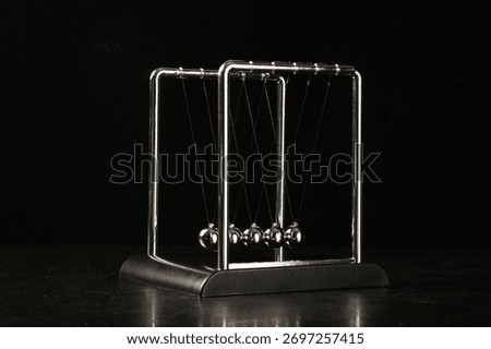 Newton's cradle pendulum physics demonstration device with chrome steel balls on black background showing motion and energy transfer principles