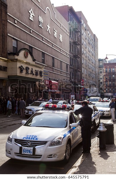 New-York, USA - NOV 18: Police officer leaning on a\
police car in a busy Chinatown street on November 18, 2012 in\
New-York, USA.