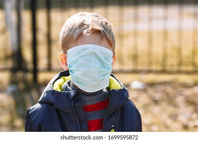 Junto a una cerca de metal está un niño con una máscara médica que le cubre completamente la cara
