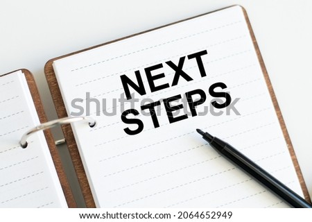 Next Steps text on notepad on table next to black marker business concept