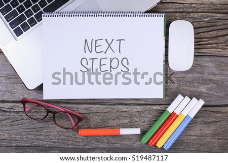 NEXT STEPS text on wooden desk with tablet pc and keyboard
