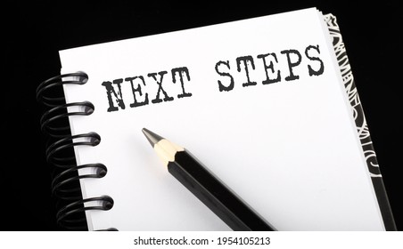 Next Steps Written Text In Small Notebook On A Black Background