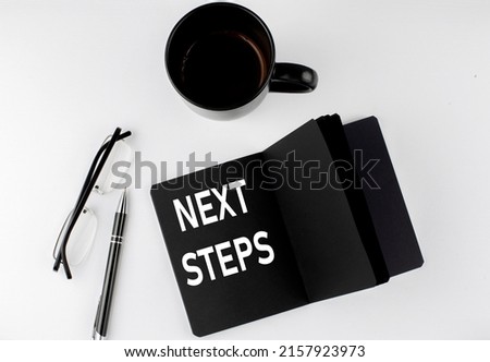 NEXT STEPS written text in small black notebook with coffee , pen and glasess on a white background. Black-white style
