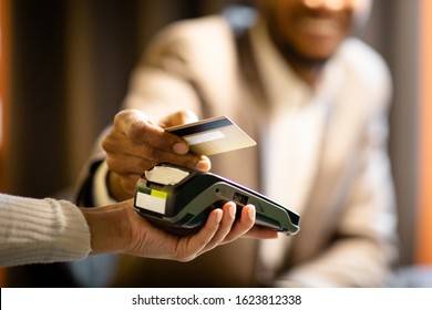 NFC Technology. Close up of black manager smiling, giving credit card to waitress paying with gold credit card in cafe - Powered by Shutterstock