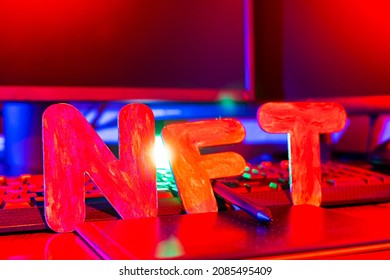 NFT ( Non-Fungible Token ) text of letters illuminated with neon light. Workplace of a graphic designer creating NFT digital art. Concept of cryptoart and blockchain technology