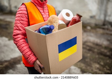 NGO volunteer carries a box with basic food and toilet papier with a Ukrianian flag sticker on the cardboard. - Shutterstock ID 2140889603