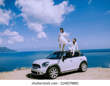 Nha Trang City, Viet Nam - May 2021: A Rich Asian Couple Sitting On The Roof Of A White Car On The Pass, Behind Is The Natural Scenery Of The Sea And The Sky. Happy Vacation.