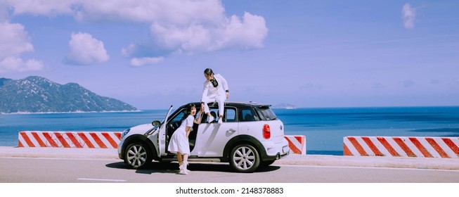 Nha Trang City, Viet Nam - May 2021: A Rich Asian Couple Sitting On The Roof Of A White Car On The Pass, Behind Is The Natural Scenery Of The Sea And The Sky. Happy Vacation.