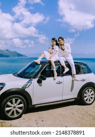 Nha Trang City, Viet Nam - May 2021: A Rich Asian Couple Sitting On The Roof Of A White Car On The Pass, Behind Is The Natural Scenery Of The Sea And The Sky. Happy Vacation.