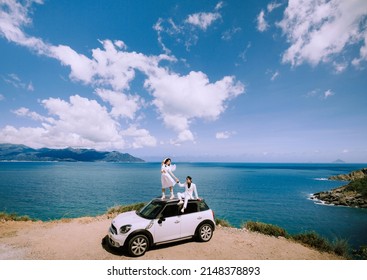 Nha Trang City, Viet Nam - May 2021: A Rich Asian Couple Sitting On The Roof Of A White Car On The Pass, Behind Is The Natural Scenery Of The Sea And The Sky. Happy Vacation.