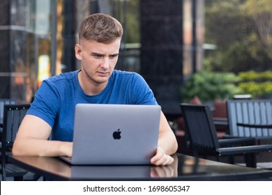 Nha Trang, Vietnam - 05.03.20: Serious Handsome Upset Guy, Freelancer, Young Sad Concentrated Focused Man Working On Laptop, Apple Computer MacBook Pro In Cafe Outdoors. Freelance Distant Job Concept