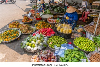 Nha Trang, Vietnam - March 11, 2019: Duong Huynh Thuc Khang market. Woman sells fresh fruits in all colors out of baskets while sittng cutting pineapple.