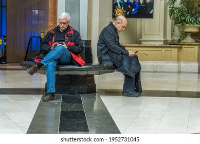 Niagara, Canada, March 2018 - Two Aged Caucasian Males Sitting At A Public Space Busy And Absorbed Checking Their Cellphones