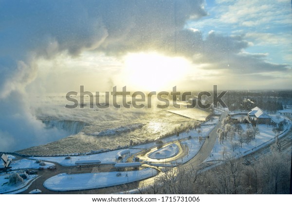 Niagara Falls in the Winter on a Cold Day with Steam\
and Mist Rising out of the Falls. Roads with few Cars. View from\
Canada to the USA