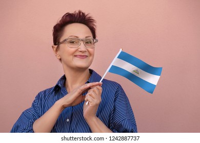 Nicaragua flag. Woman holding Nicaragua flag. Nice portrait of happy middle aged lady 40 50 years old with a national flag over pink wall background on the street outdoors.