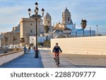 nice, active senior woman cycling with her electric mountain bike at the waterfront of old moorish city of Cadiz, Andalusia, Spain