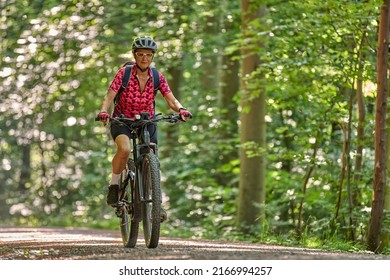 nice active senior woman riding her electric mountain bike in the green city forest of Stuttgart, Germany