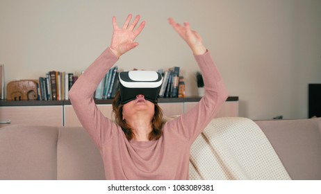Nice Adult Lady is Using VR Glasses with Raised Arms Trying to Touch Virtual 3D Objects at Home