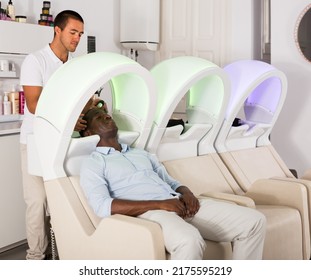 Nice African American Man Leaning Heads On Sink And Relaxing .while Hairdresser Washing His Hair In Barbershop