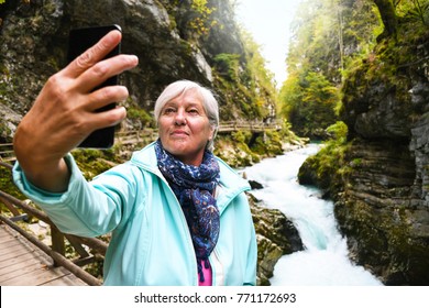 Nice Attractive Elderly Mature Woman With Shiny Grey Hair Taking Photos And Selfies Outdoor In A Vintgar River Canyon Gorge On A Beautiful Sunny Autumn Day