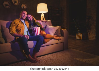 Nice attractive lovely cheerful cheery couple girl sitting on divan enjoying snack watching film spending day weekend holiday at night dark home house apartment indoors