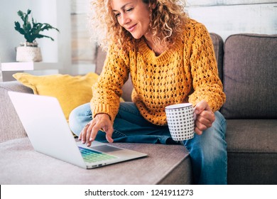Nice beautiful lady with blonde curly hair work at the notebook sit down on the sofa at home - check on oline shops for cyber monday sales - technology woman concept for alternative office freelance - Shutterstock ID 1241911273