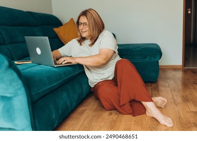 Nice beautiful woman in glasses working at the notebook near the sofa at home. Concepts of education, work and comfort. 30s female working indoors - Powered by Shutterstock