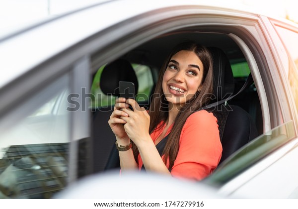 Nice beautiful young woman smile and use\
mobile phone touching the screen inside the car while travel.\
modern concept of search hings and contact friends when you are\
away. daily use of\
smartphone