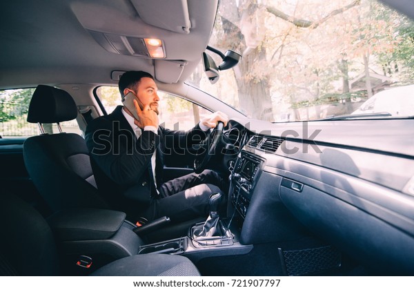 Nice\
business talk. Handsome young businessman talking on his smart\
phone and smiling while sitting on the front\
seat