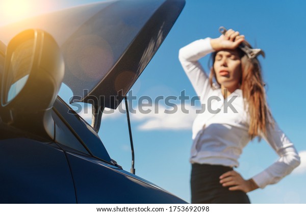 Nice business woman standing upset while repairing\
an engine with a wrench. Broken car. Accident with an auto.\
selective focus.