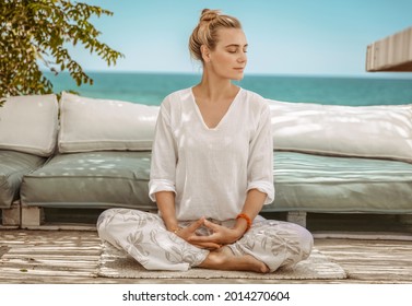 Nice Calm Female With Closed Eyes Sitting In Lotus Pose On The Terrace Of Beach House. Meditating On The Beach. Zen Balance. Peaceful Summer Vacation.