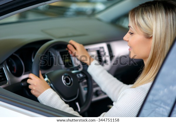 Nice car.\
Pleasant cheerful delighted woman sitting at the wheel while\
choosing auto in auto show and going to buy\
it