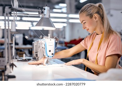 nice caucaian blonde textile factory worker on production line using modern sewing machine, at workshop. hardworking young woman engaged in sewing or tailoring, dressmaking concept - Powered by Shutterstock