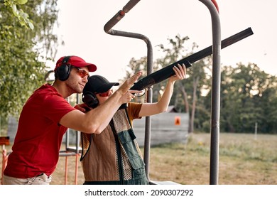 Nice caucasian male in headset is confidently teaching woman to use rifle, weapon on outdoor range, Handsome male and pleasant lady in protective clothes equipment outfit learning to shoot