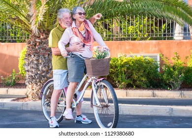 Nice Caucasian Senior Adult Couple Have Fun Going And Moving On A Vintage Bike Together. Woman Carry A Man On An Old Bicylcle In Outdoor Leisrue Happy Activities. Nice Lifestyle Retired People