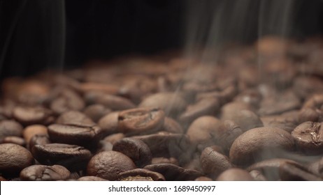 Nice and cinematic footage of roasted coffee beans. Camera slowly fly above coffee beans with smoke with black background.