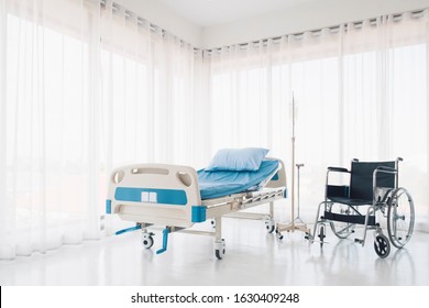 Nice and Clean Hospital bed with pillow, blanket, intravenous (IV) stand and wheel chair, No patient in the room in the modern hospital. Healthcare, medical insurance concept.