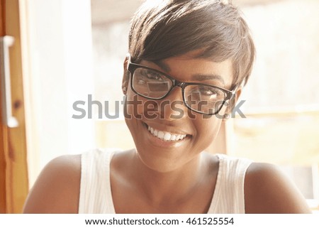 Nice close-up portrait of young girl in geeky glasses with pixie cut. Intelligent Spanish woman with shinny smile and brown eyes happily looking at camera. Successful lifestyle concept and happiness.