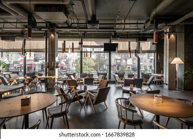 Nice coffee house in a loft style with big panoramic windows and concrete columns. There are round wooden tables with chairs and armchairs, glass coffee bean dispensers, TV, light floor lamp. - Shutterstock ID 1667839828