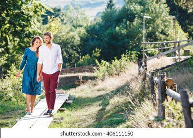 Nice couple walking together, outdoor, in the countryside. Beloved holding hands of each other and smiling. Girl looking down and man looking straight. Full body