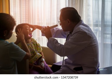 Nice Doctor Hole Flashlight And Using Hand Touching Face For Prove Oral And Neck From Young Patient Boy Who Open Mount And Sticking Tongue Out For Diagnose With Radiant Sunlight In Hospital Room.