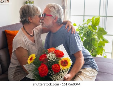 Nice Elderly Couple At Home. They Embrace And Kiss To Celebrate Valentine's Day With A Large Bouquet Of Flowers