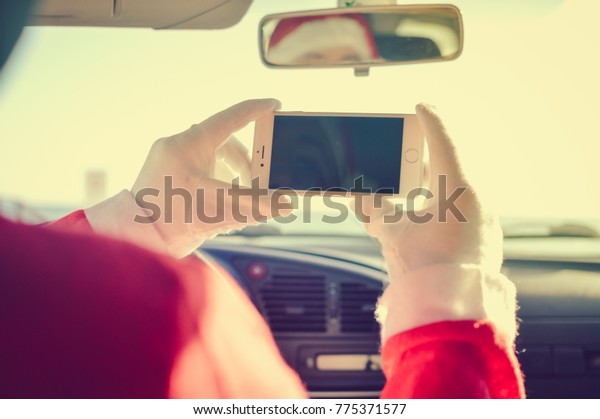 Nice, France - 06 December 2017: Closeup on\
driving car Santa Claus using Apple Iphone 8 smartphone online\
mockup background. Joyful tradition celebration, busy season\
delivering time, outdoors\
window