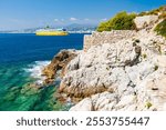 NICE, FRANCE:  ferry boat arriving at the harbour, from Corsica and Sardinia, sailing past the rocky coastal path and transparent sea water, French Riviera of Mediterranean Sea