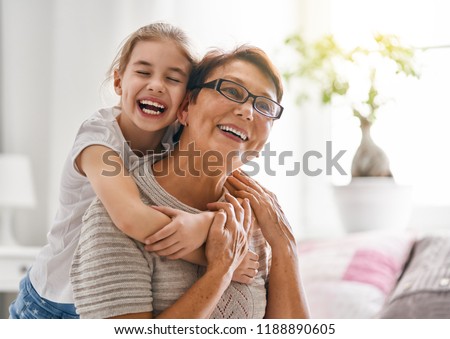 A nice girl and her grandmother enjoy sunny morning. Good time at home. Family playing in the bedroom.