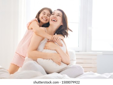 A Nice Girl And Her Mother Enjoy Sunny Morning. Good Time At Home. Child Wakes Up From Sleep. Family Playing On The Bed In The Bedroom.