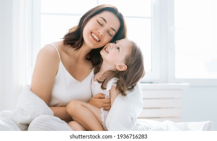 A Nice Girl And Her Mother Enjoy Sunny Morning. Good Time At Home. Child Wakes Up From Sleep. Family Playing On The Bed In The Bedroom.   