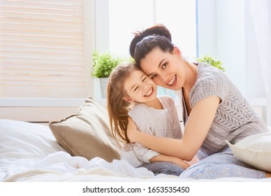 A nice girl and her mother enjoying sunny morning. Good time at home. Child wakes up from sleep. Family playing on the bed in the bedroom.   - Shutterstock ID 1653535450