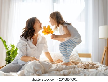 A nice girl and her mother enjoying sunny morning. Good time at home. Child wakes up from sleep. Family playing on the bed in the bedroom. - Powered by Shutterstock